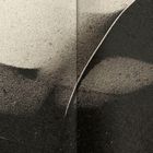 Das Bild zeigt eine sandige Oberfläche in hellen und dunklen Tönen, mit geschwungenen Linien und Schatten.
