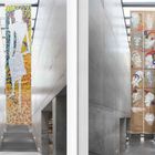 Links: Buntes Gemälde mit stilisierter weißer Figur. Rechts: Spiralförmige Zeichnungen von Köpfen. Beide hängen in Betonflur.