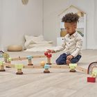 Ein Kind spielt auf dem Boden mit einer Holzbahn. Buntes Spielzeug umgibt es in einem schlicht eingerichteten Raum.