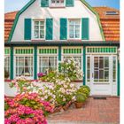 30 JUL/AUG, MO 26 DI 27 MI 28 DO 29 FR 30 SA 31 SO 01. Haus mit grünem Rahmen, Blumen im Vorgarten.