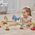 Ein Mädchen liegt am Boden und spielt mit einer Murmelbahn aus Holz mit bunten Elementen. Im Hintergrund ein Korb mit Kuscheltieren.