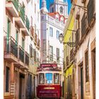 31 AUGUST. Historische rote Straßenbahn in einer engen, farbenfrohen Straße mit Balkonen, Kirchtürme im Hintergrund.