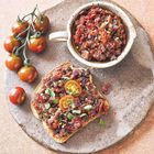 Keine erkennbaren Texte. Ein Teller mit Bruschetta, garniert mit Tomaten und Basilikum, daneben ein Zweig Kirschtomaten.