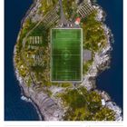 25 So, 29. Woche 2027, JULI.  
Ein Fußballfeld auf einer felsigen Insel, umgeben von Wasser, mit parkenden Autos und Grünflächen.