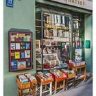 Text: "Antiquariat" und "Türkenstr. 37". Bücher in Holzkisten vor einem Antiquariat. Kalendereintrag: "32 AUGUST".