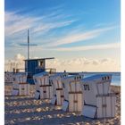 August 32, Strandkörbe mit Nummern, Rettungsstand 5.50. Sandiger Strand, blauer Himmel und ruhige See im Hintergrund.