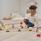 Ein Kind sitzt lachend auf dem Boden. Vor ihm ist ein Holzspielzeug aufgebaut. Im Hintergrund gemütliches Kinderzimmer.