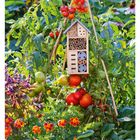 "33 AUGUST" unten, ein Insektenhotel an einem Tomatenstrauch mit reifen Tomaten und bunten Blumen im Garten.