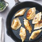 Gebratene Teigtaschen in einer schwarzen Pfanne, daneben eine Schale mit Sojasauce und Kräutern.
