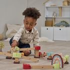 Ein Kind spielt auf dem Boden mit einer bunten Holzkugelbahn in einem hellen Raum mit Regalen und Kissen.