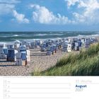 33. Woche, August 2027. Strandkörbe auf Sandstrand, mit grünem Gras und blauem Himmel, Wolken und Meer im Hintergrund.