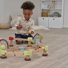 Ein Kind spielt auf dem Boden mit einer Holzeisenbahn. Im Hintergrund sind Regale mit Spielzeug.