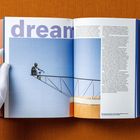 „dream“ in großen Buchstaben. Ein Mann sitzt entspannt auf einer Metallstruktur vor blauem Himmel. Seite eines Buches.