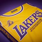Buchcover mit gelbem Lakers-Basketballtrikot, Titel: "AN OFFICIAL HISTORY OF THE PURPLE & GOLD". Seiten: "TASCHEN".