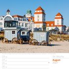 Historische Strandwagen am Binzer Strand vor einem weißen Haus mit roten Dächern und mehreren Türmen; August 2027.