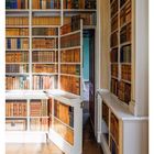 Geheimtür in der Bibliothek, umrahmt von Holzregalen voller Bücher. Holzboden reflektiert Licht. Kalenderdaten unten.