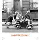 Text: "Kinder in einer Seifenkiste - Großbritannien - 1950er-Jahre." Drei Jungen fahren lachend in einer Seifenkiste.