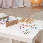 Eine Schachtel mit Montessori-Spielzeug, darunter farbige Kugeln, liegt auf einem Tisch mit Lochbrett und Punktkarten.
