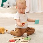 Ein kleiner Junge sitzt auf einem Teppich und spielt mit buntem Holzspielzeug. Im Hintergrund sind Kissen zu sehen.