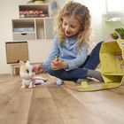 "Nice" auf einem gelben Koffer. Ein Mädchen spielt mit einer Spielzeugkatze auf einem Holzboden. Im Hintergrund ein Regal.