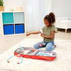 Ein Kind sitzt auf einem Teppich und spielt mit einem Arztkoffer. Im Hintergrund ein Regal mit bunten Boxen.