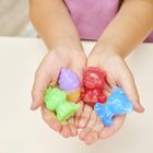 Kleine Hände halten bunte Wachsfiguren: grün, lila, rot und blau, in Tier- und Kegel-Formen.