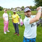 Drei Männer auf einem Golfplatz. Einer trägt ein Shirt mit "GOLF COACH", ein anderer zeigt einen Golfschwung.