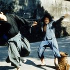 Zwei Personen kämpfen auf einer Straße, beide in Kampfposen. Ein Korb liegt am Boden. Im Hintergrund sind Schatten sichtbar.