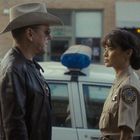 Zwei Personen: ein Mann mit Cowboyhut, Ledermantel, und eine Frau in Polizeiuniform neben einem Streifenwagen.