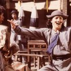 Zwei Männer in traditioneller Kleidung, einer trägt einen Hut. Sie scheinen in einer fröhlichen Geste zu interagieren.