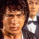 Zwei Männer, vorderer mit zerzaustem Haar und entschlossenem Gesichtsausdruck, der andere im Anzug unscharf im Hintergrund.