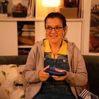 Ein Plakat mit der Aufschrift „d'Auvergne“ im Hintergrund. Eine Person mit Brille hält ein blaues Objekt, sitzt auf einem Sofa.