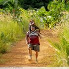 Ein Mann in zerrissener Kleidung rennt auf einem Feldweg, während er ein Wildschwein auf den Schultern trägt.