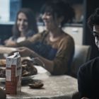 Ein Mann sitzt nachdenklich am Tisch, im Hintergrund lachen drei Frauen. Eine Saftpackung steht auf dem Tisch.