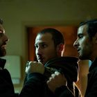 Drei Männer in intensiver Diskussion in einem Raum mit gedämpftem Licht.