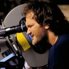 Nicht erkennbarer Text, ein Mann schaut durch eine große Filmkamera, fokussiert und konzentriert.