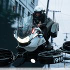 Text: "EMERGENCY CALL 911". Eine Polizistin auf einem fliegenden Motorrad vor unscharfem Hintergrund.