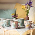 Tassen mit Texten "Kleine Auszeit" und "Zeit für mich", verziert mit Blumen und Schmetterlingen. Im Hintergrund Blumen.