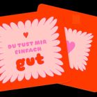 „DU TUST MIR EINFACH gut“ in bunten Buchstaben vor einem blumenförmigen Hintergrund mit Herzmotiv.