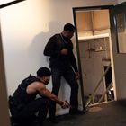 Zwei Männer in taktischer Kleidung stehen vor einer halb offenen Tür. Einer kniet und hält eine Waffe, der andere steht.