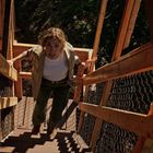 Eine Frau mit hellem Shirt steigt eine steile hölzerne Treppe hoch, umgeben von Maschendrahtzaun.