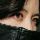 Es gibt keinen sichtbaren Text. Nahaufnahme von Augen hinter einem schwarzen Lederkragen, mit schwarzem Haar.