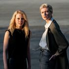 Zwei Personen stehen draußen. Die linke hat langes blondes Haar, die rechte kurzes blondes Haar und trägt eine Jacke.