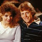 Ein Mann und eine Frau lächeln gemeinsam in einer gemütlichen Umgebung. Sie tragen 80er-Jahre-Mode.