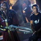 Zwei Personen in futuristischer Kleidung, links in Rüstung mit Maske und langen Klingen, rechts in schwarzem Shirt mit Gerät.