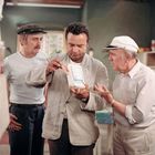 Eine Packung mit dem Text "Farina" und "Poudre" wird von drei Männern betrachtet.