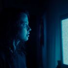 Eine Person schaut auf einen Fernseher mit blauem Bildschirmrauschen. Der Raum ist dunkel.