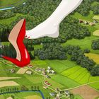 Ein großer Fuß in einem roten Schuh schwebt über einer üppigen Landschaft mit Wäldern, Feldern und einer Kirche.