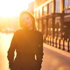 Eine Frau steht in einer sonnendurchfluteten Straße, die Sonnenstrahlen erzeugen eine warme, goldene Atmosphäre.
