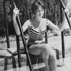 Eine Frau in einem gestreiften Bikini sitzt auf einer Poolleiter. Sie lächelt und hält sich an den Handläufen fest.